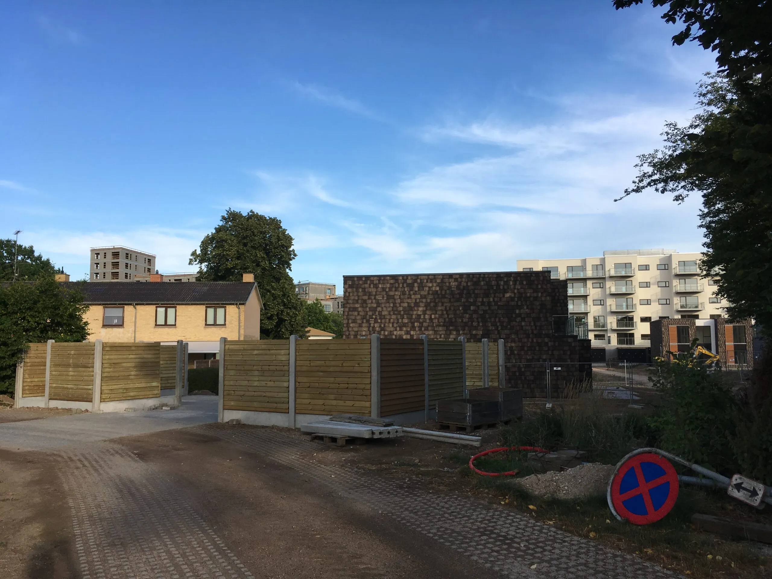 Byggeplads med nyt træhegn og nyopførte lejligheder i baggrunden, standsning forbudt-skilt i forgrunden