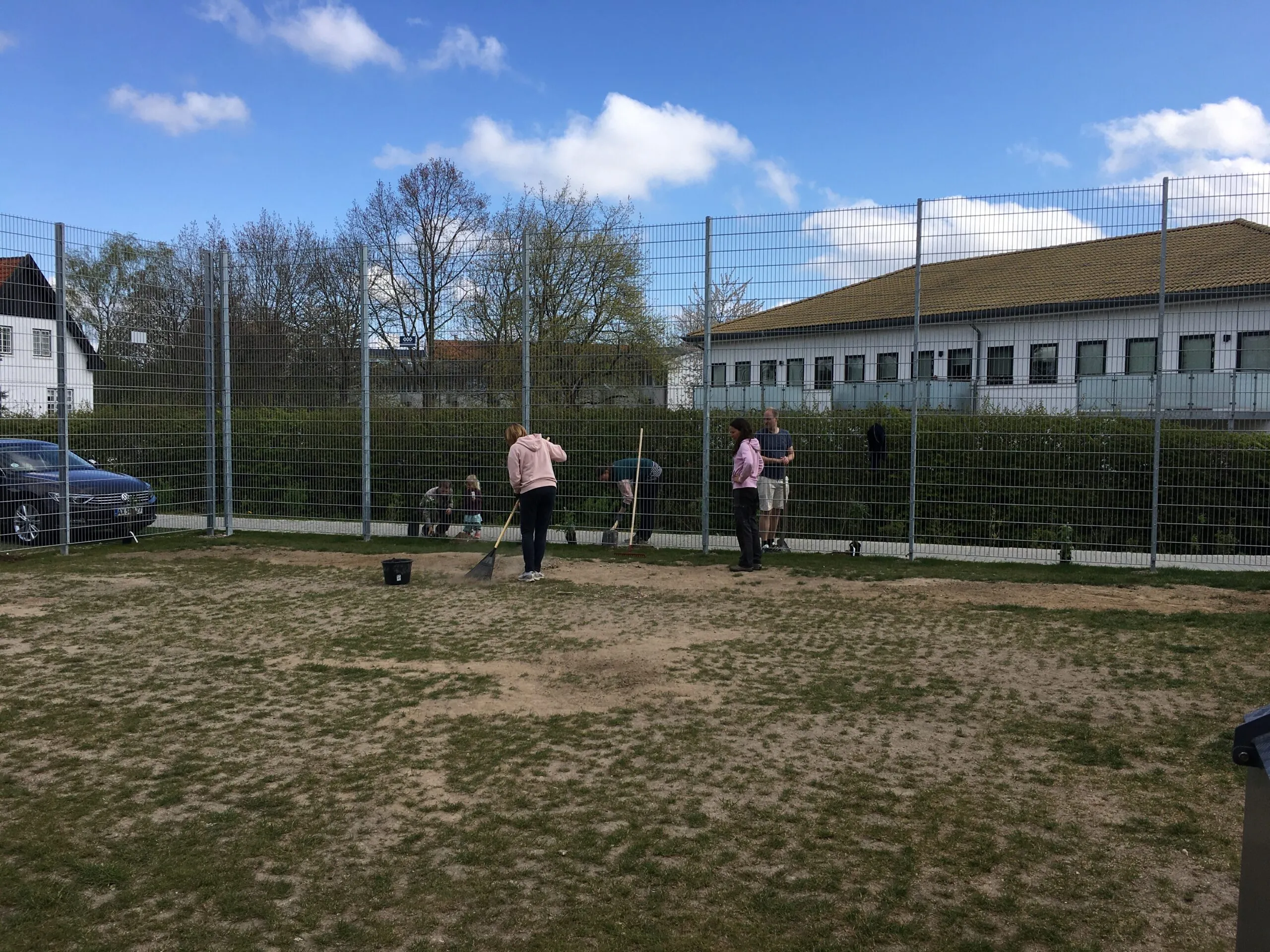 Beboere river og rydder op på boldbanen bag hegn en solrig forårsdag