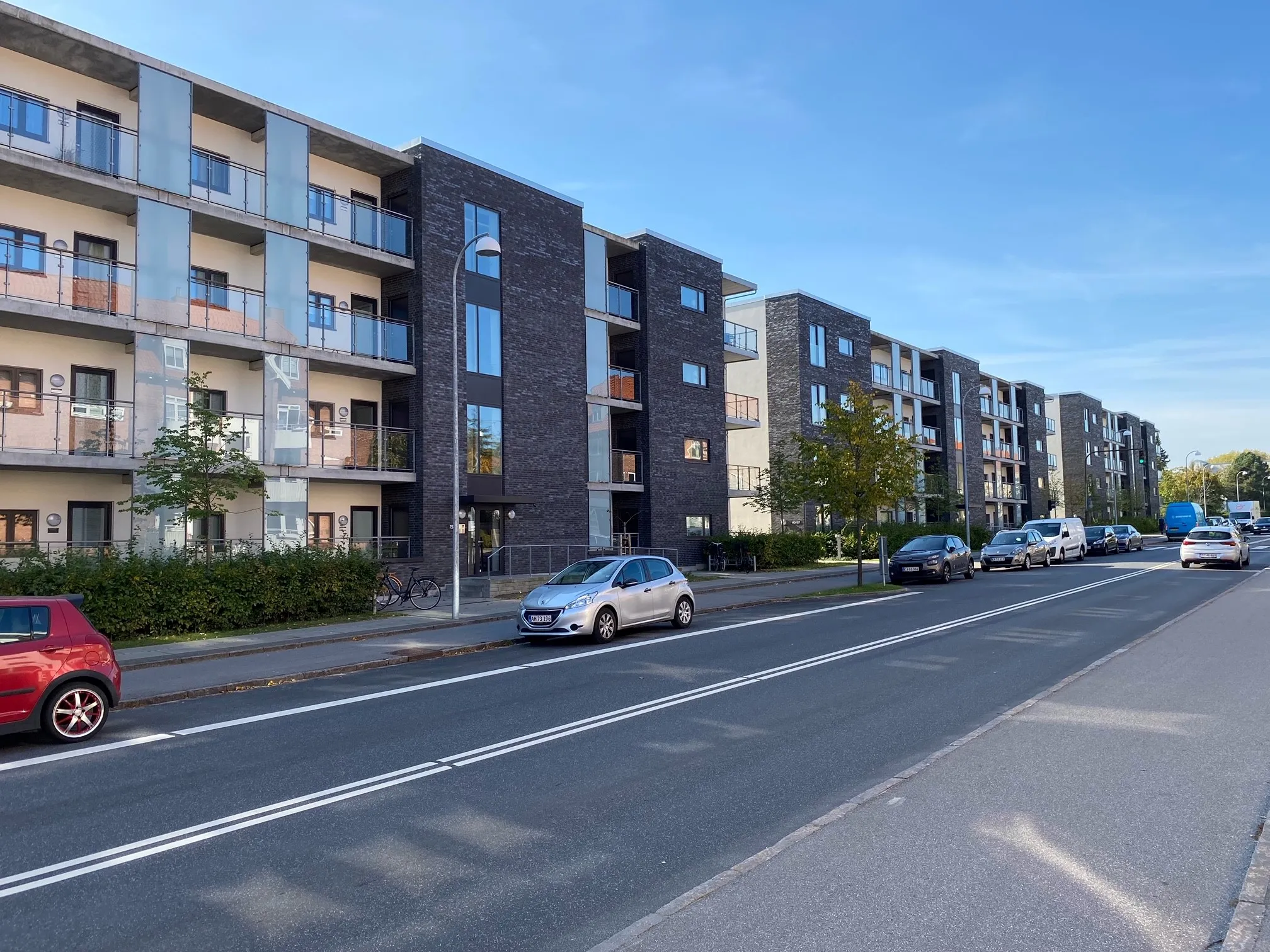 Moderne lejlighedsbygninger i mørke mursten med altaner set fra vejen med parkerede biler